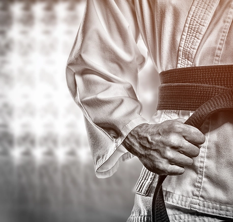 Une personne vêtue d'un kimono de arts martiaux tient fièrement sa ceinture noire, sur un fond flou de lumières, exprimant force et concentration.